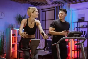 Man and woman engaging in Zone 2 heart rate training on treadmills in a well-equipped, contemporary gym setting